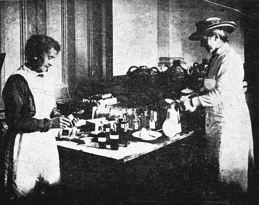 Medicine department at the Wellington Town Hall during the 1918 influenza epidemic. Shows where the standard mixture and tonic were prepared and bottled. Mrs. Waters (right) was in charge. Taken by an unidentified photographer. Reproduced from New Zealand Free Lance: 1/2-C-016207-F, 1918, Alexander Turnbull Library: National Library of New Zealand, Wellington, New Zealand.