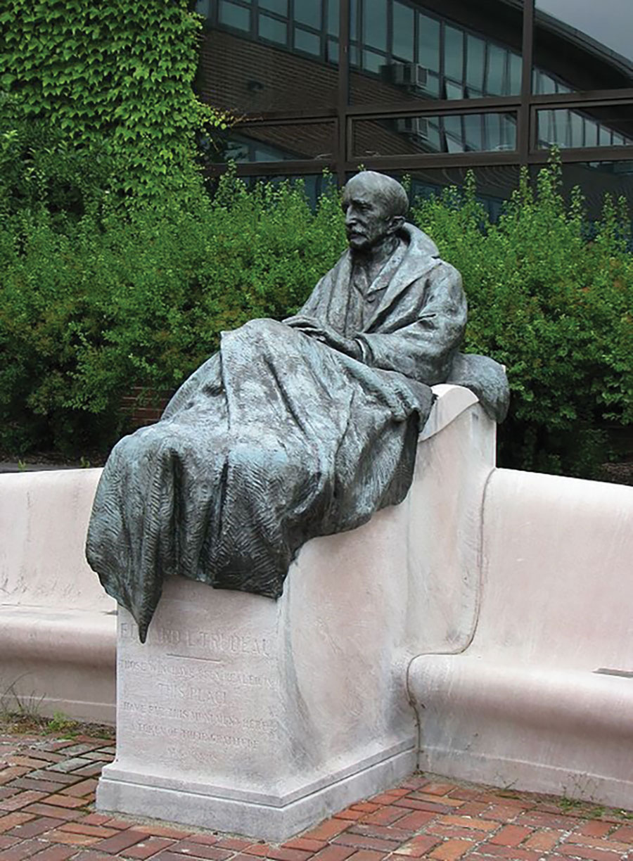 Gutzon Borglum. Statue of E.L. Trudeau, 1918. Bronze. From Historic Saranac Lake Wiki. Originally erected at the Adirondack Cottage Sanatorium. Moved to the Trudeau Institute, Saranac Lake, New York, 1964. The statue is a representation of E. L. Trudeau as a male tuberculosis patient with a blanket folded on his lap. In the pedestal is an inscription with a folk-saying favorite of Trudeau, “Guerir quelquefois, soulager souvent, consoler toujours” (To cure sometimes, to relieve often, to comfort always). Trudeau started the facility, which has been credited with being the first sanatorium in the United States, at Saranac Lake in 1885, at the dawn of the nation’s sanatorium movement, which peaked with over 108,000 beds in 1954. Sanatoriums remained the standard of care for tuberculosis for over half a century in the United States; after streptomycin was discovered in 1943 and antimicrobial drugs were subsequently used to treat and cure tuberculosis, sanatoriums closed or were transformed into general hospitals. 