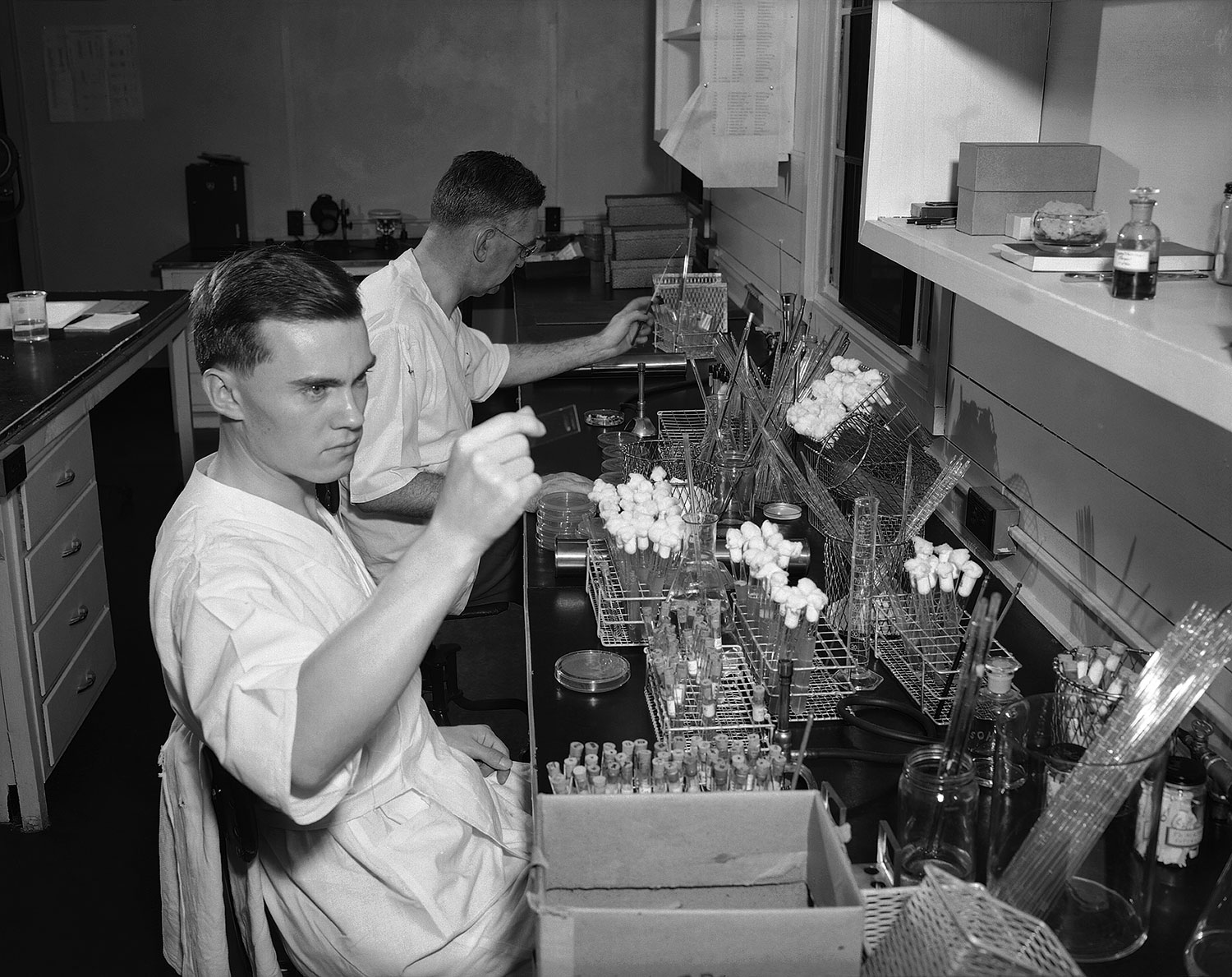 Dr. P.R. Edwards of the US Public Health Service seated in the background, and George Herman working in the Enteric Bacteriology Unit Laboratory. Dr. Edwards joined the staff of the Communicable Disease Center of the Public Health Service in 1948 and served as Chief of the Enteric Bacteriology Unit until June 1962, when he accepted the post of Chief of the Bacteriology Section at CDC. Image source: Public Health Image Library. 