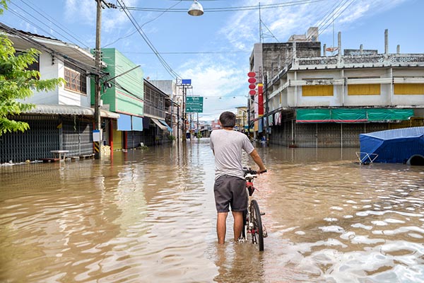 man walking bike through floodwaters