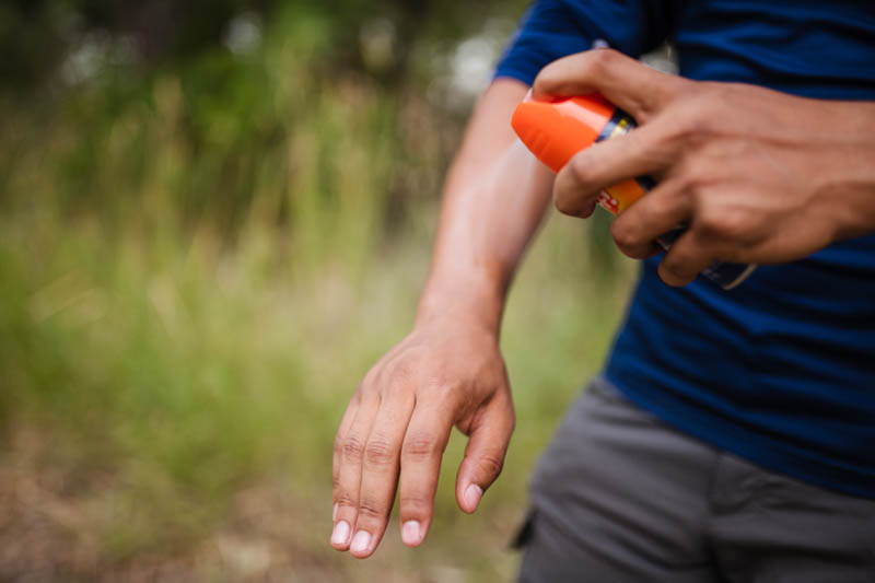 Person spraying insect repellent on arms