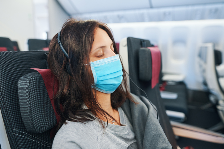 woman in a mask sleeping on a plane